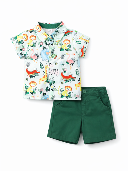 白背景のスタジオ撮影で、子ども用2点セットをフラットレイで配置。動物や植物柄の半袖ボタンシャツ（ライトブルー系）と、ダークグリーンのショートパンツを組み合わせたデザイン。
