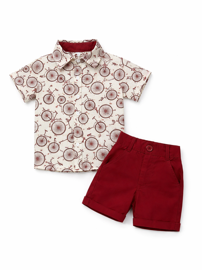 白背景のスタジオ撮影で、男の子用2点セットをフラットレイで配置。自転車柄の半袖ボタンシャツ（クリーム系）と、ボルドーのショートパンツを組み合わせたデザイン。
