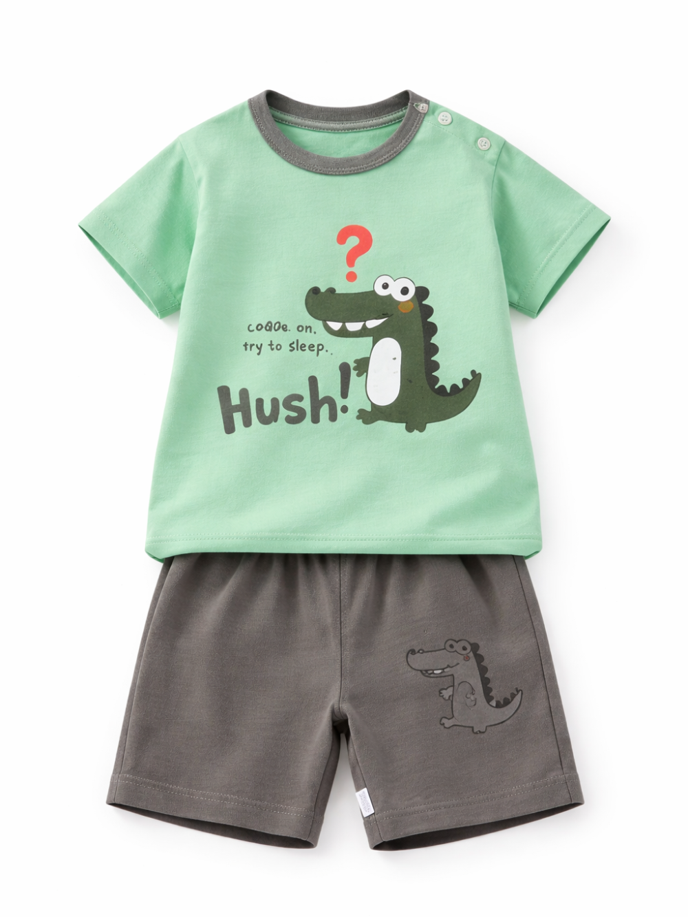 白背景のスタジオ風商品写真。ミントグリーンの半袖Tシャツとチャコールグレーのショートパンツの上下セットが、正面向きにきれいに配置されている。Tシャツはグレーの襟ぐりと肩のスナップボタン付きで、赤い「？」とワニのイラスト、「Hush!」の文字がプリント。パンツはウエストがゴム仕様で、裾側に小さなワニのプリントが入っている。
