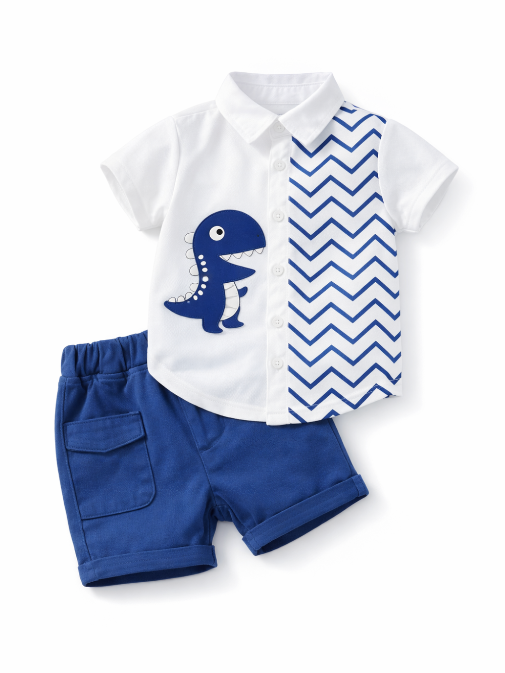 白背景のスタジオ風商品写真。男の子用の上下セットが斜めに配置されている。白い半袖シャツは襟付きで前開きボタン、左側に青い恐竜のアップリケ、右側に青のジグザグ（シェブロン）柄の切り替えデザイン。下はロイヤルブルーのショートパンツで、ウエストはゴム仕様、片側にフラップ付きポケットがあり、裾は折り返しになっている。
