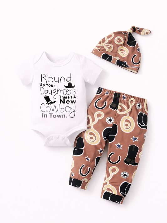 白背景のスタジオ風商品写真。ベビー用の3点セットがフラットに配置されている。左に白い半袖ロンパースがあり、フロントにカウボーイ風の英字フレーズと帽子・ブーツのアイコンがプリントされている。右下にブラウン地のロングパンツが置かれ、投げ縄、ブーツ、馬蹄などのカウボーイモチーフが総柄で入っている。右上に同柄の結び目付きベビーハットが配置されている。
