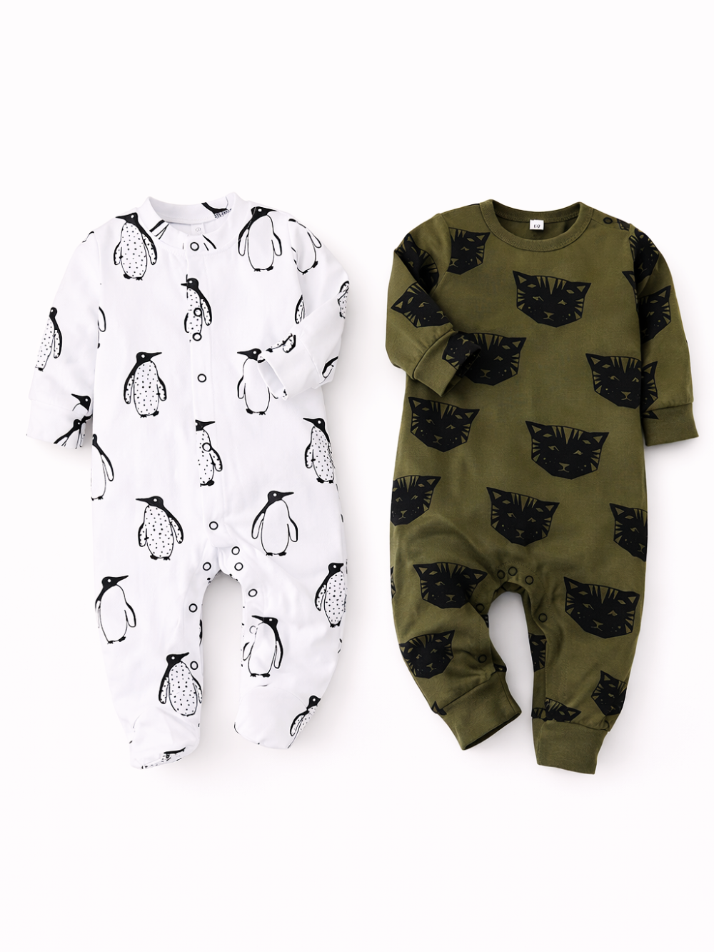 白背景に、ベビー用の長袖ロンパースが2着並んでいる。左は白地にペンギン柄の足つきロンパース、右はカーキ地に黒いネコの顔柄の足なしロンパース。やわらかな影がつき、縫製や生地の質感がはっきり見える。
