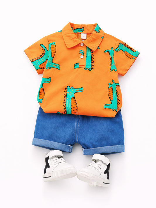 白背景のスタジオで、ワニ柄のオレンジ色ポロシャツとデニムショートパンツ、白いハイカットスニーカーを並べた子ども用コーディネートの俯瞰写真。
