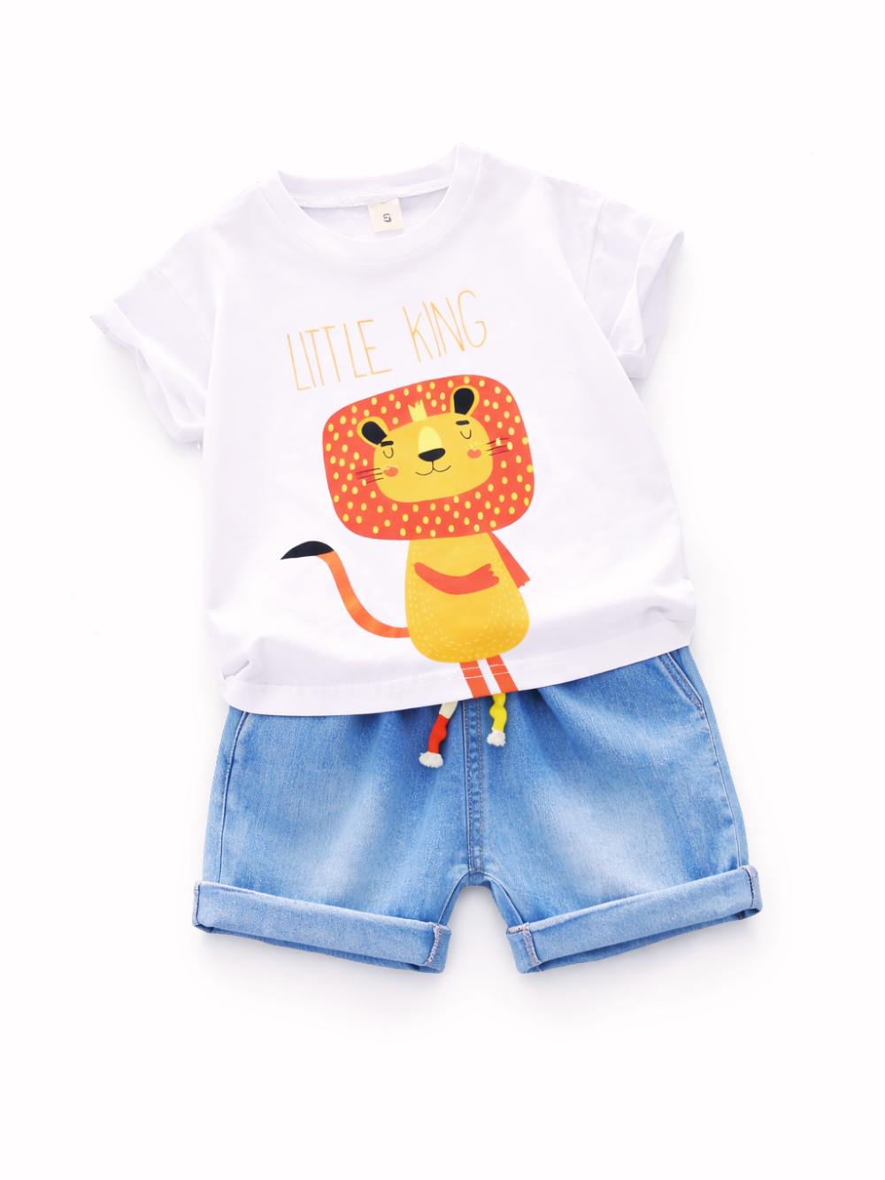 白背景に、子ども用の夏コーデ（白いTシャツ＋デニムショーツ）がフラットレイで整然と配置されている。Tシャツにはライオンのイラストと「LITTLE KING」の文字、ショーツは裾を折り返したライトブルーで、ウエストにカラフルな飾り紐が付いている。
