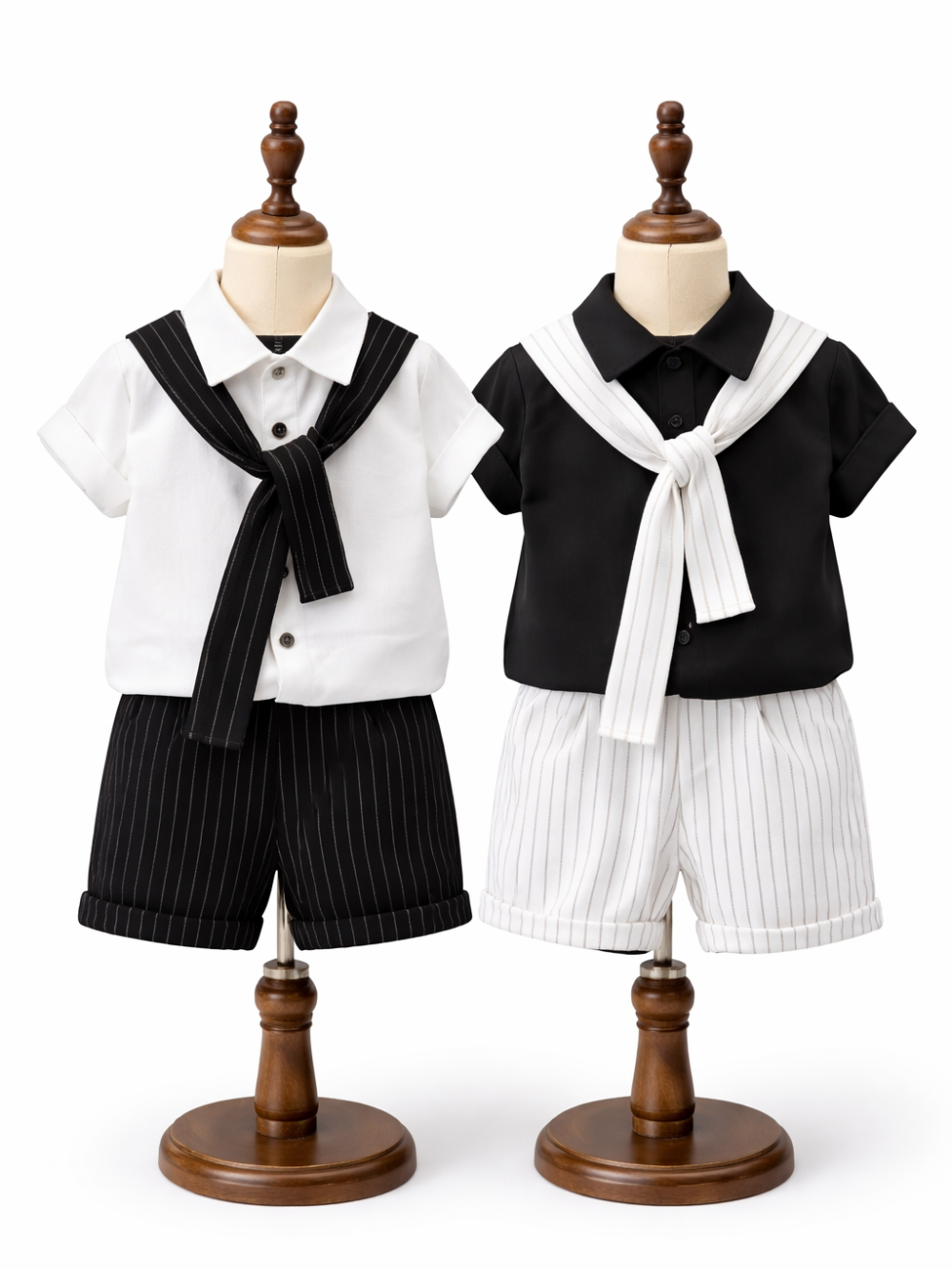 白背景のスタジオで、木製トルソーに掛けたキッズ用セーラー風セットアップ2着（左：白シャツ＋黒スカーフ＋黒ピンストライプ短パン、右：黒シャツ＋白スカーフ＋白ピンストライプ短パン）が並んでいる。
