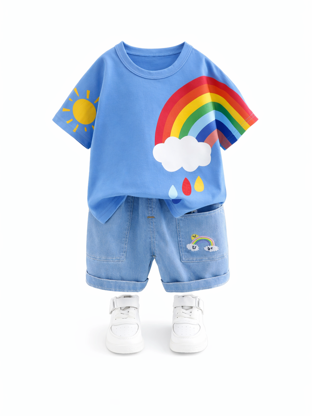 白背景に、子ども用の上下セット（空色のTシャツとデニム風ショートパンツ）が中央に整然と配置されている。Tシャツ右側に虹と雲のプリント、左袖に太陽のプリントがあり、パンツ右ポケット付近にも小さな虹のワンポイントが入っている。
