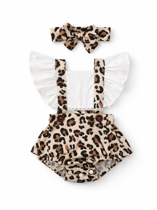 白背景に、ベビー用のサスペンダー付きロンパースとヘアバンドが平置きで配置されている。ロンパースは白い身頃に大きなフリル袖が付き、レオパード柄のサスペンダーとスカート風のバブルボトムが組み合わさっている。ウエスト部分にブラウンのボタンが2つあり、股下にはスナップボタンが付いている。上部には同じレオパード柄の大きなリボンヘアバンドが置かれている。全体が均一な光で撮影され、輪郭と素材感がはっきり見える。
