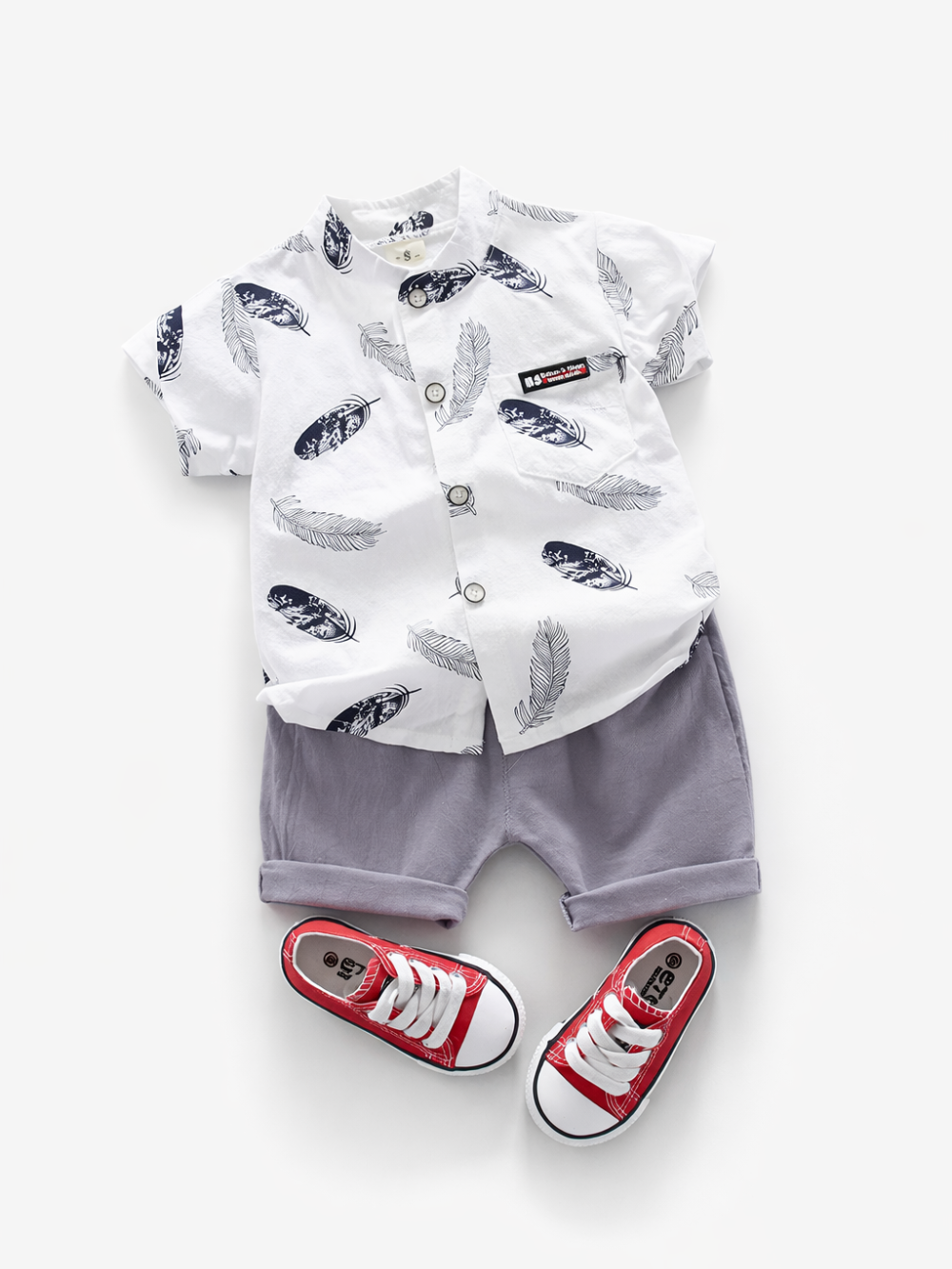 白背景にフラットレイで並べた男の子用夏コーデ。羽根柄の白い半袖ボタンシャツとラベンダーグレーのショートパンツ、赤いキャンバススニーカー。
