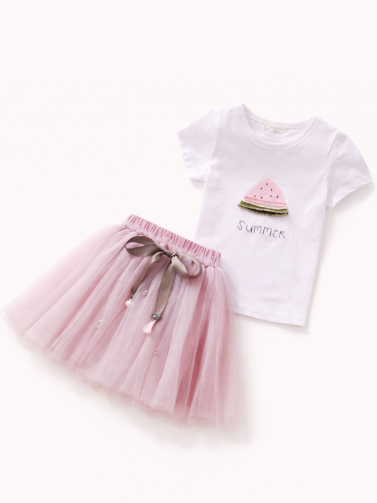 白背景に平置きされた女の子用2点セット。スイカモチーフの白Tシャツと、リボン付きの淡いピンクのチュールスカート。
