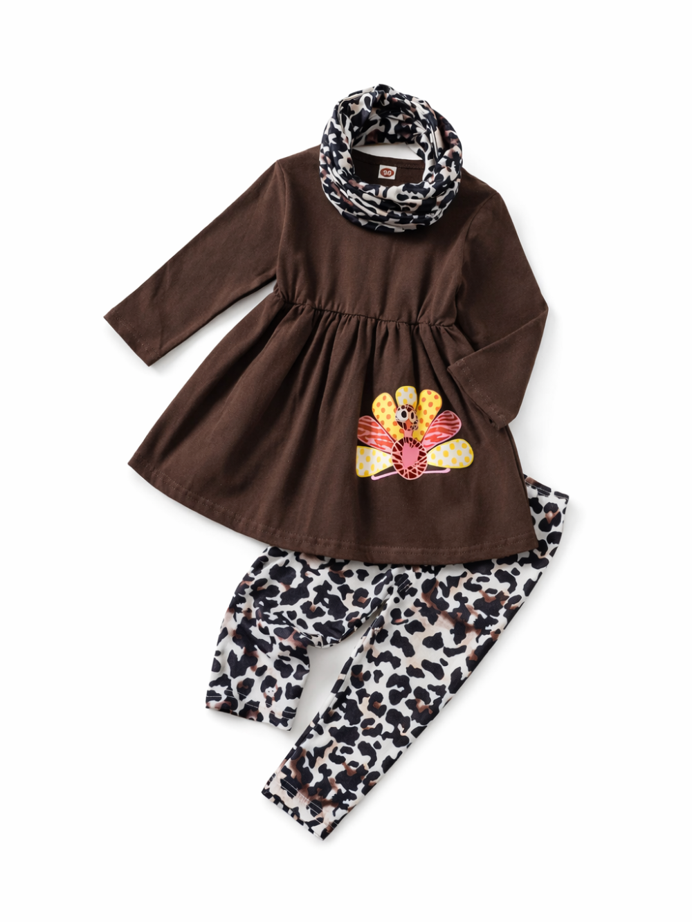白背景に、子ども用の3点セットが平置きで写っている。ブラウンの長袖ワンピース（前身頃にカラフルなモチーフ付き）に、白黒のレオパード柄レギンスと同柄のスヌードが合わせてある。
