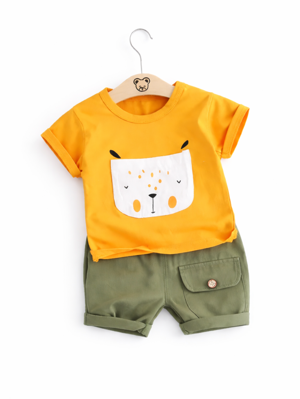 白背景に掛けたキッズ用上下2点セット。イエローの半袖Tシャツ（動物フェイスのポケット風プリント）と、カーキグリーンのショートパンツ（折り返し裾・フラップポケット付き）を並べている。
