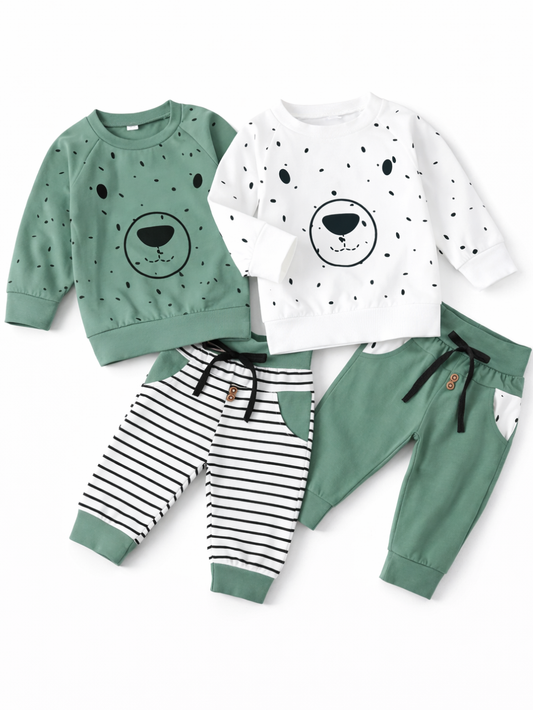 白背景に並べたキッズ用スウェット上下セット2種類。左はグリーンのくま顔プリントトレーナー＋白黒ボーダーのパンツ、右は白地ドット柄のくま顔プリントトレーナー＋グリーンのパンツで、いずれもリブ袖・裾とウエスト紐付き。

