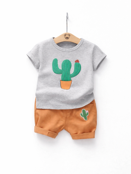 白背景に木製ハンガーで掛けたキッズ半袖セットアップ。グレーのサボテンプリントTシャツと、サボテンワッペン付きオレンジのショートパンツ。

