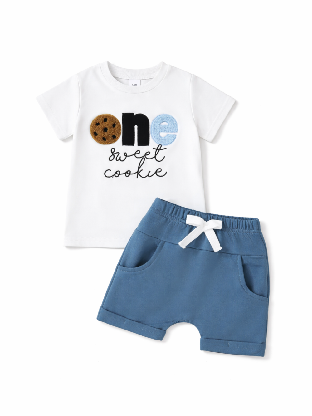 白背景に配置されたベビー用上下2点セット。白い半袖Tシャツに「one sweet cookie」の文字デザイン（クッキー風の“O”を含む）が入り、ブルーのショートパンツはウエストゴムと白いリボン紐、ポケット付き。
