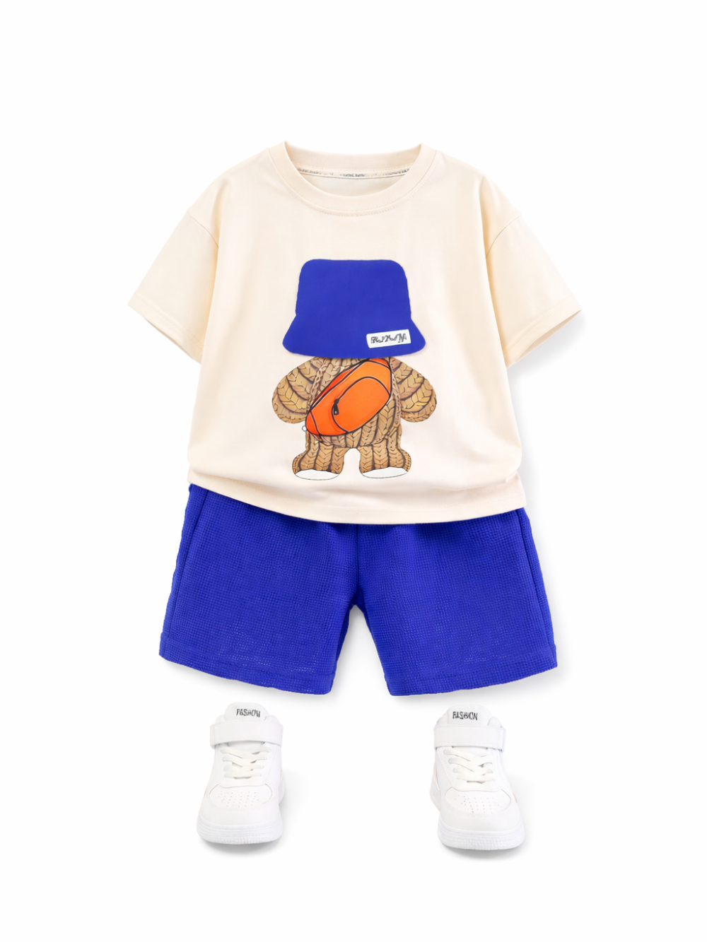白背景に配置されたキッズ用上下セット。生成り色の半袖Tシャツに、青いバケットハットとオレンジのバッグを身に着けたキャラクターのプリント。ロイヤルブルーのメッシュショートパンツと白いスニーカーが合わせてある。
