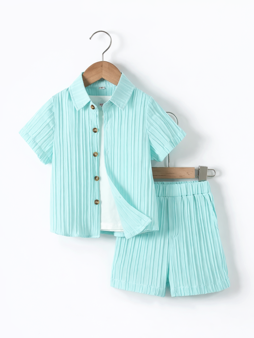 白背景にハンガー掛けされたキッズ用上下セット。ミントグリーンのプリーツ素材の半袖ボタンシャツ（木目ボタン、前が少し開いて白インナーが見える）と、同素材のウエストゴムショートパンツが並んでいる。やわらかな影で立体感がある。
