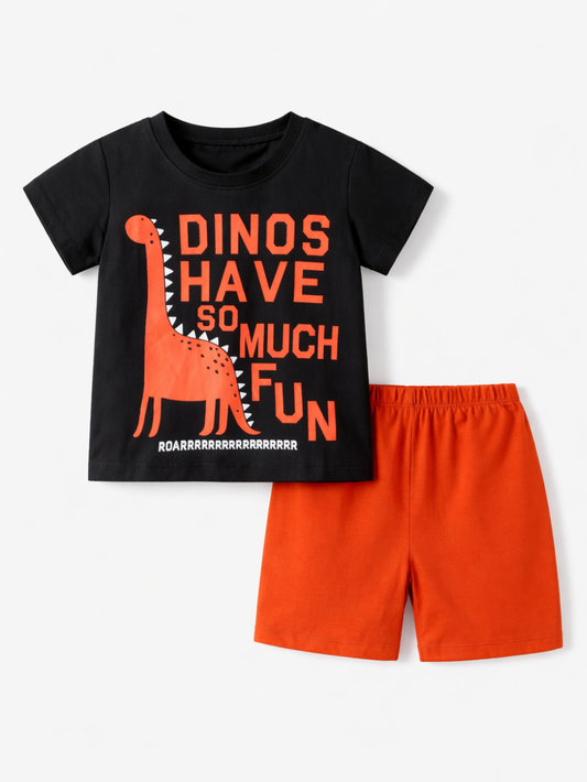 白背景に平置きされたキッズ用上下セット。黒の半袖Tシャツにオレンジの恐竜イラストと「DINOS HAVE SO MUCH FUN」の文字が大きくプリントされており、右下にオレンジのショートパンツが並べられている。やわらかな影で立体感がある。
