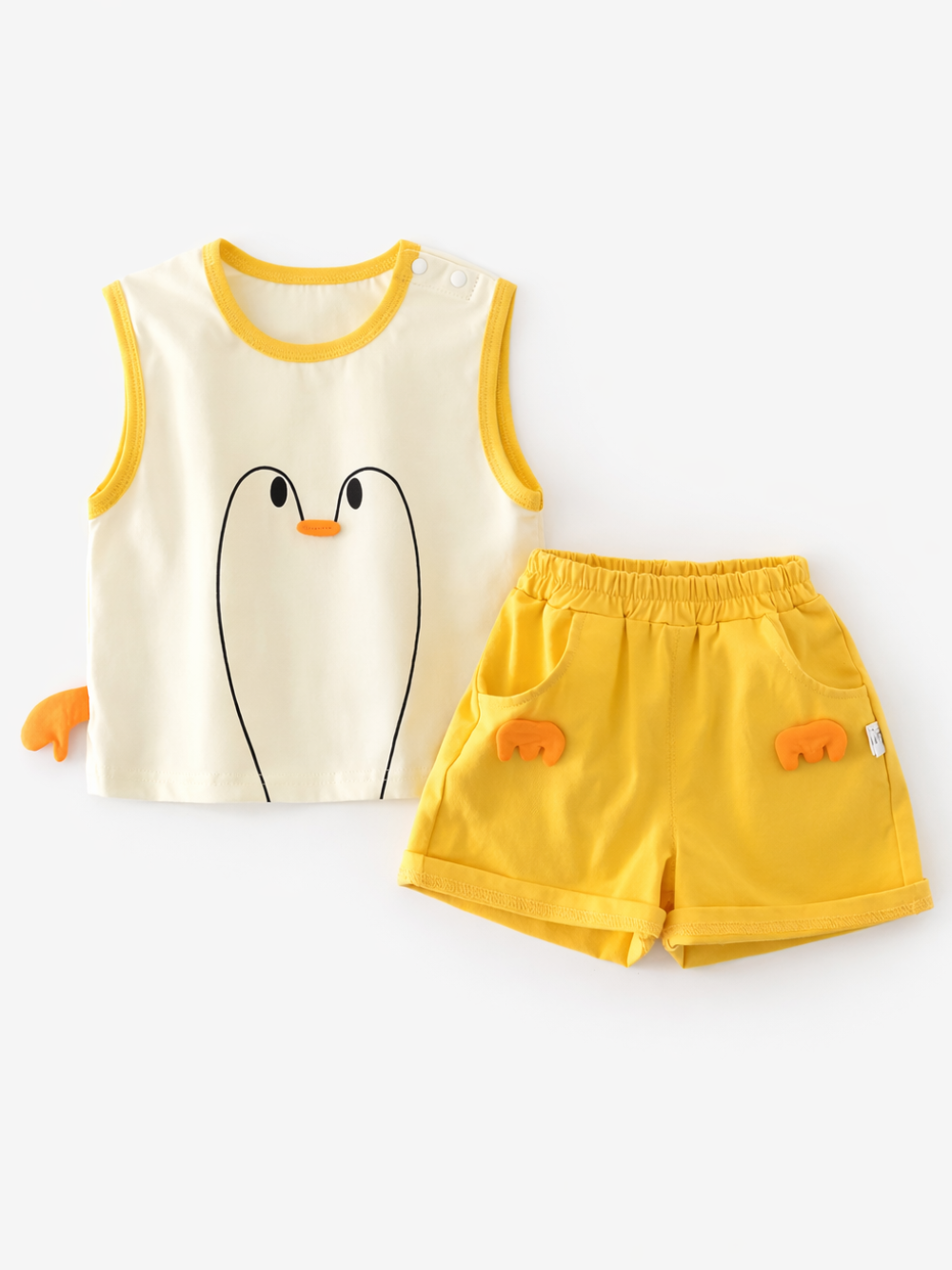 白背景に平置きされたキッズ用上下セット。クリーム色のノースリーブトップスにシンプルなペンギンの顔デザイン（黒い線の目とオレンジのくちばし）があり、サイドにオレンジのひれ状パーツが付いている。右側にイエローのウエストゴムショートパンツが配置され、ポケット部分にオレンジのひれ状飾りが付いている。やわらかな影で立体感がある。
