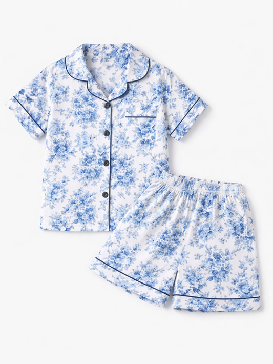 白地に青い花柄の子ども用半袖パジャマ上下セット（前開きシャツ＋ショーツ）を白背景でフラットレイ撮影した商品画像。
