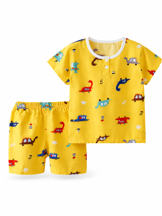 子ども用半袖トップス＆ショートパンツの2点セット。イエロー地に恐竜や乗り物の総柄プリント。白背景のスタジオ撮影で、トップスとパンツを並べて見せている。
