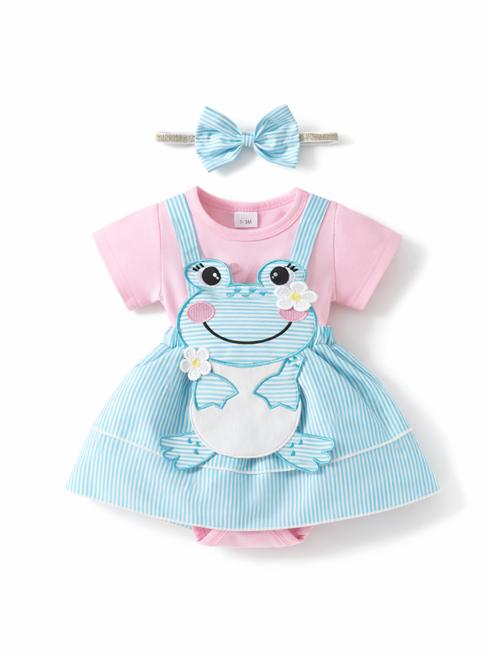 ベビー用ワンピース風ロンパースとヘアバンドの2点セット。ピンクの半袖ボディに、水色×白ストライプのジャンパースカートを重ねたデザインで、前面にカエルのアップリケと小花モチーフ付き。上部に同柄リボンのヘアバンド付き。白背景のスタジオ撮影。
