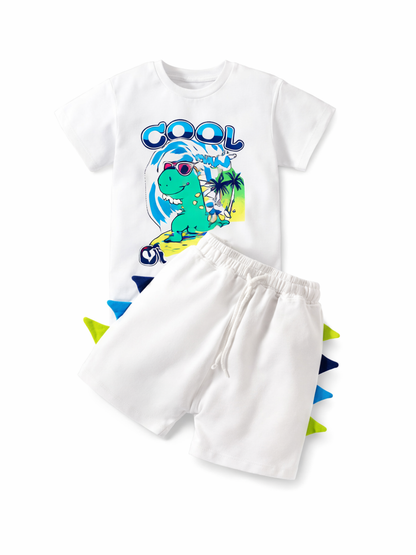 白いキッズ用半袖Tシャツとショートパンツの2点セット。Tシャツ正面にサングラスをかけた恐竜のカラフルなプリント、パンツ脇に青・紺・黄緑のスパイク装飾があり、白い背景に平置きで撮影されています。
