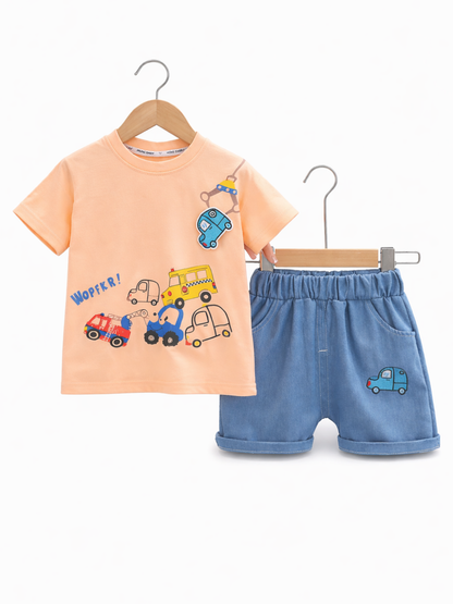 ピーチカラーのキッズ半袖Tシャツとライトブルーのショートパンツの2点セット。Tシャツには車のイラストプリント、パンツには小さな車のワッペンがあり、ハンガーに掛けて白背景で撮影されています。

