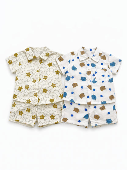 キッズ用の半袖シャツ＆ショートパンツの2セットを並べた商品画像。左はアイボリー地にカーキの星柄、右は白地に青と茶色の動物柄プリントで、白背景に平置き撮影されています。
