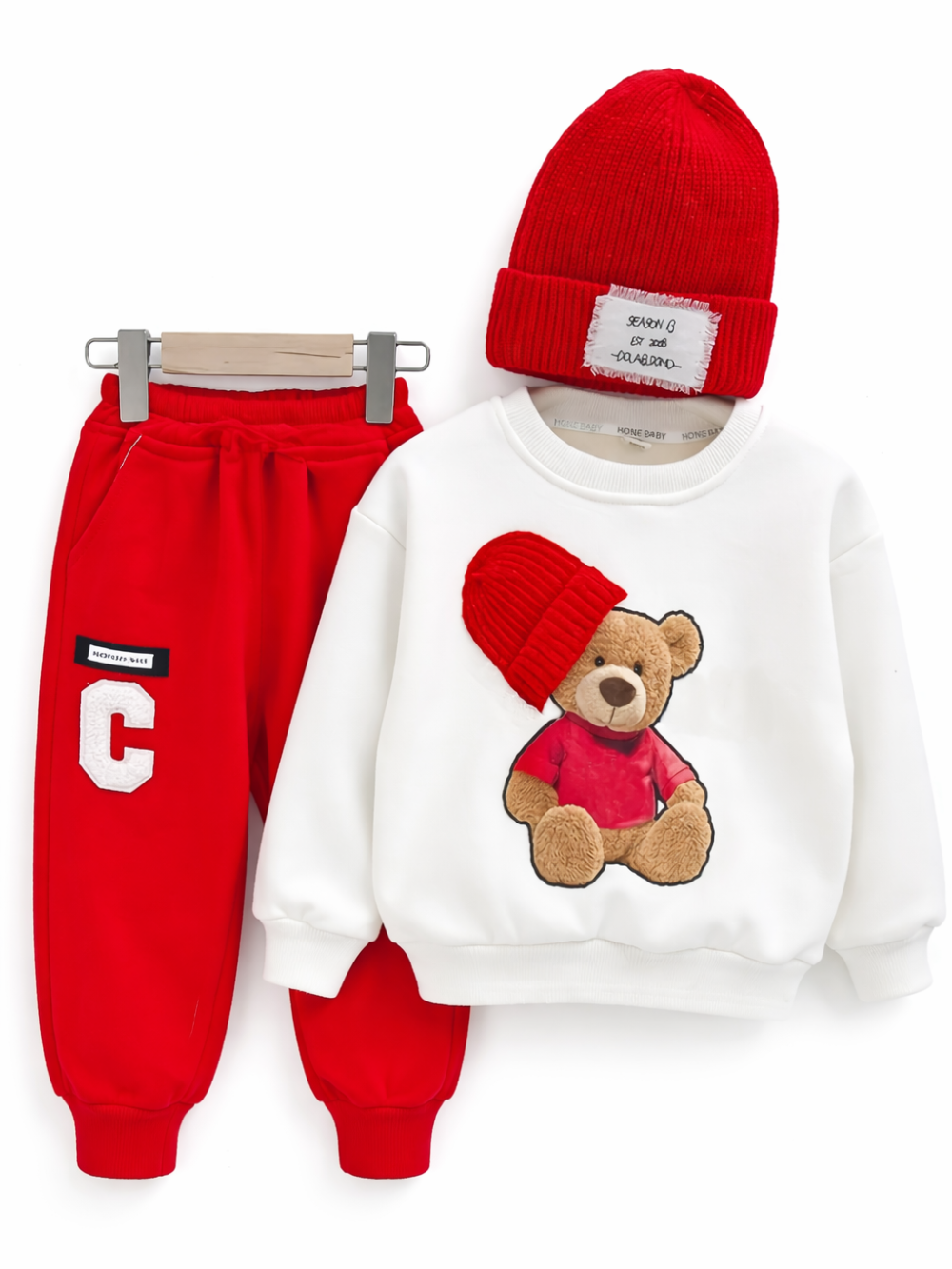 キッズ用の3点セット。白いトレーナーは赤い帽子をかぶったクマのアップリケ付きで、赤いスウェットパンツと赤いニット帽がセットになっています。白背景でハンガー掛けのように配置して撮影されています。
