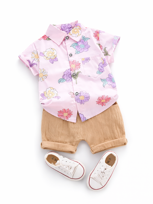 キッズ用コーディネート。淡いピンクの花柄半袖シャツとベージュの折り返しショートパンツ、白いキャンバススニーカーを白背景に平置きで撮影しています。
