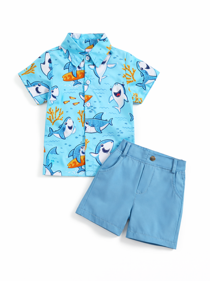 キッズ用の半袖シャツとショートパンツの2点セット。水色のシャツにサメや魚、サンゴのイラスト柄プリント、無地の水色ショーツはポケット付き。白背景に平置きで撮影されています。
