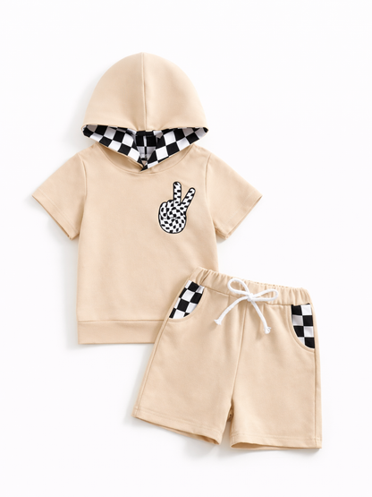 キッズ用の半袖フーディーTシャツとショートパンツの2点セット。ベージュ生地に、フード内側とポケットが白黒チェック柄、胸にピースサインのワッペン付き。ウエストはゴムと白い紐で、白背景に平置き撮影されています。
