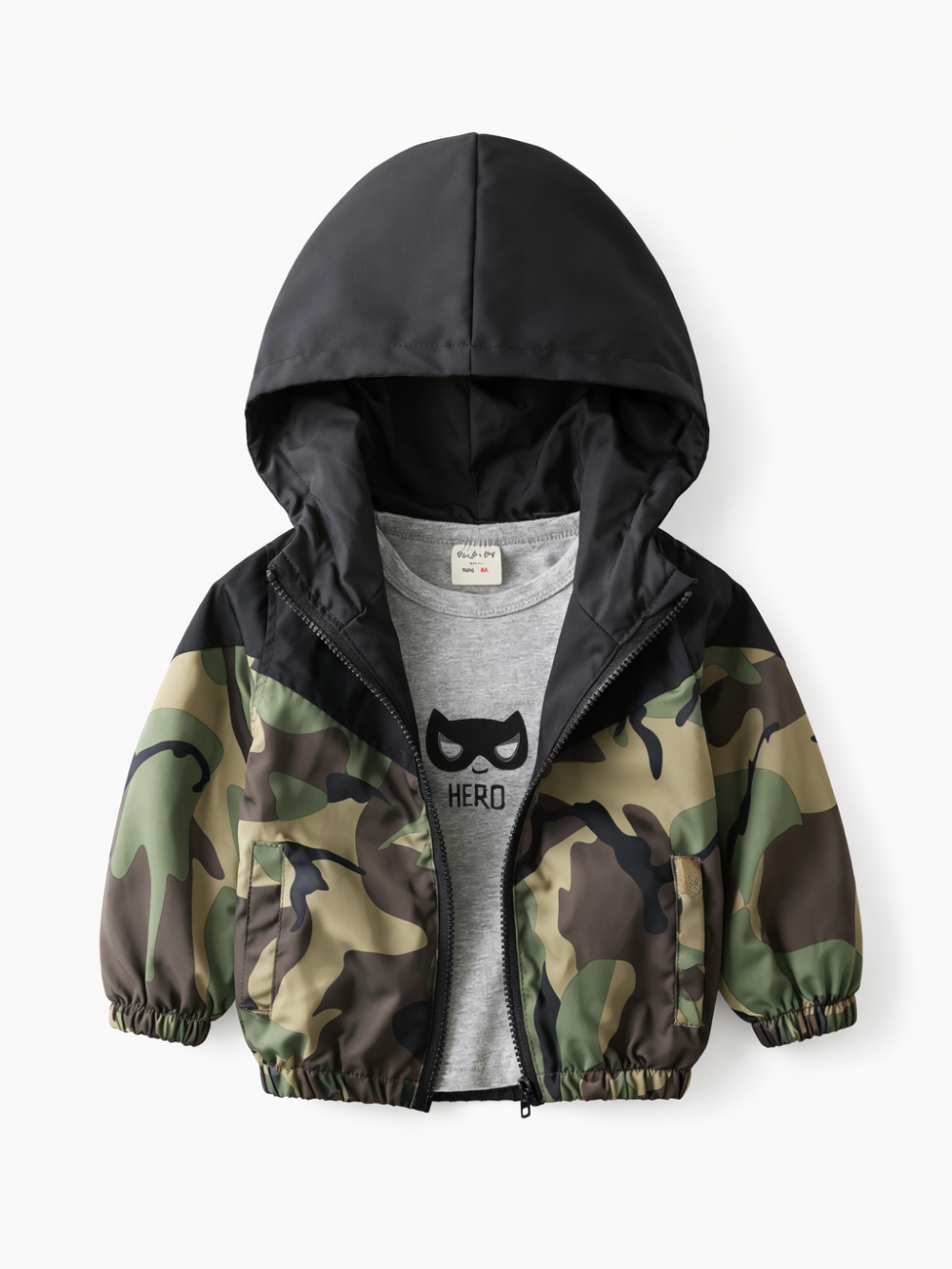 白い背景に、黒いフード付きカモフラージュ柄のキッズジャケットが置かれている。前は少し開いており、中のグレーTシャツに「HERO」のプリントが見える。
