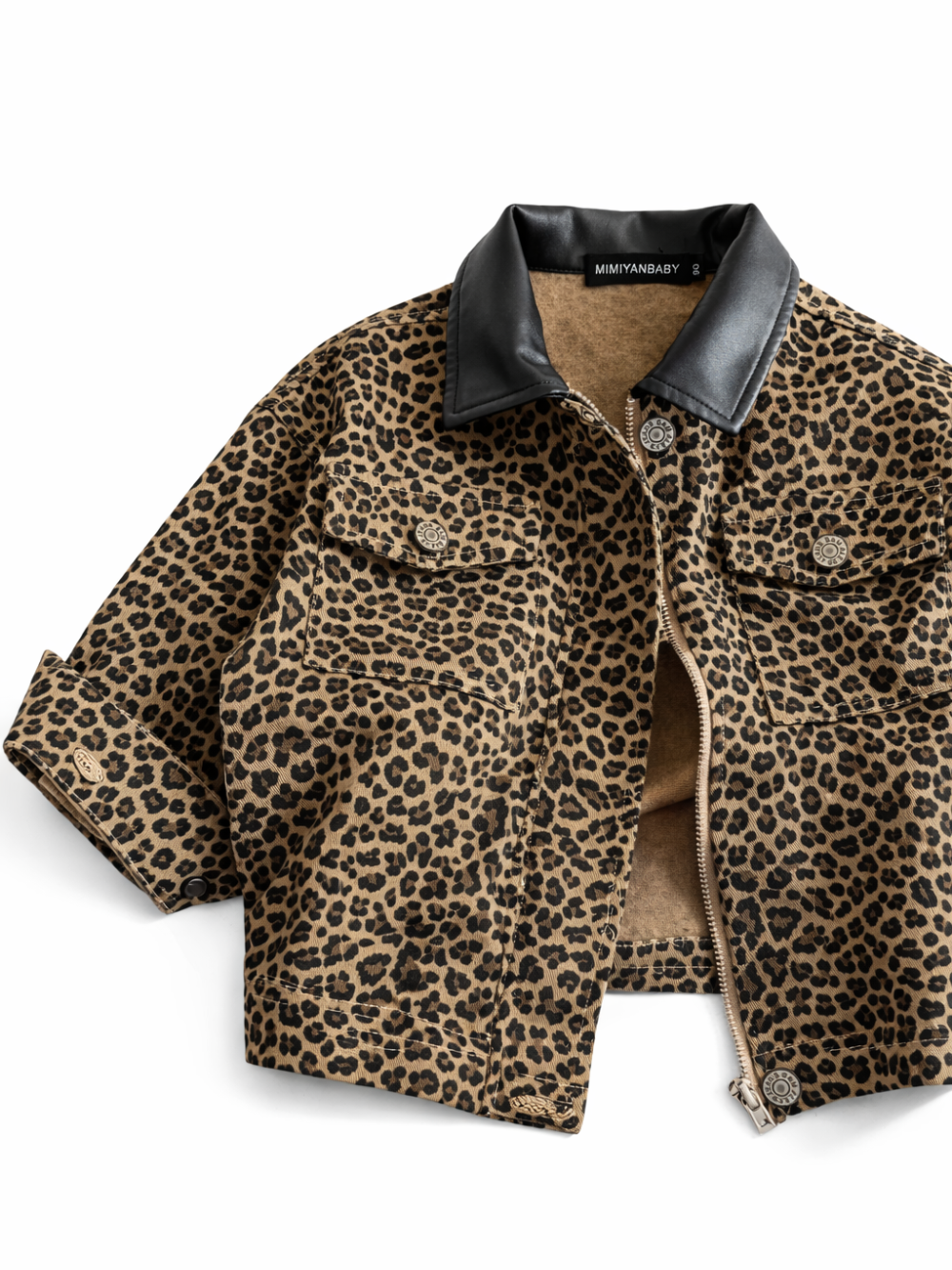 ヒョウ柄のクロップド丈ジャケットのフラットレイ。黒のフェイクレザーカラー、フロントジップ、胸ポケットとメタルボタンが見える。白いスタジオ背景に均一な光で撮影され、やわらかな影が入っている。
