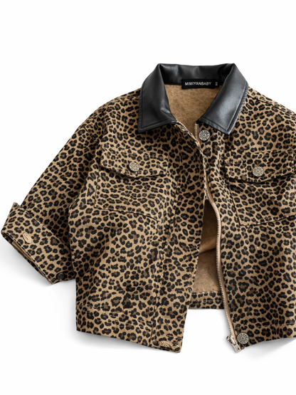 ヒョウ柄のクロップド丈ジャケットのフラットレイ。黒のフェイクレザーカラー、フロントジップ、胸ポケットとメタルボタンが見える。白いスタジオ背景に均一な光で撮影され、やわらかな影が入っている。
