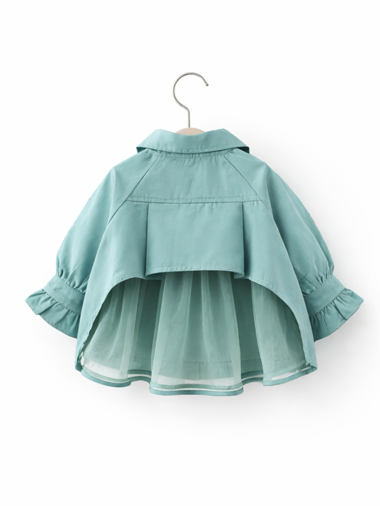 ミントグリーンの子ども用アウターをハンガーに掛けた背面写真。背中にヨーク切り替えがあり、裾はチュールのレイヤーでふんわり広がる。袖口はギャザー入りのフリル。白いスタジオ背景で均一な光、やわらかな影が入っている。
