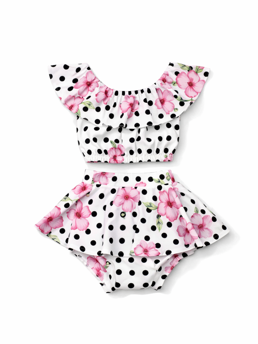 白地に黒の水玉とピンクの花柄が映える、フリル襟のショートトップスとスカート風ブルマの女の子用2点セット。スタジオの純白背景で、質感がくっきり見える高精細な商品写真。
