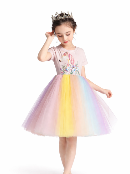 王冠をつけた女の子が、ユニコーン柄のトップスとパステルカラーのチュールスカートのドレスを着てポーズをとる、白背景のカタログ風商品画像。
