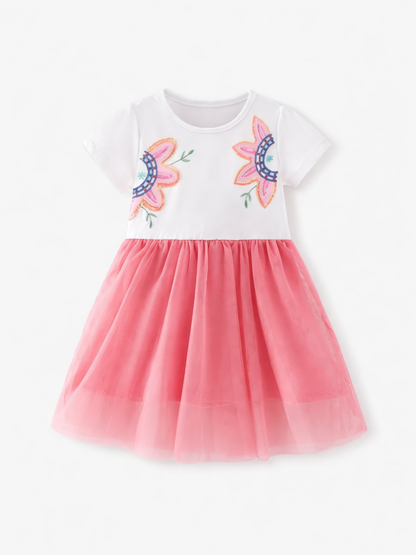 白い半袖トップに胸元の花刺繍、ピンクのチュールスカートを重ねた子ども用ワンピース。正面から、真っ白な背景で均一な照明と自然な薄い影。
