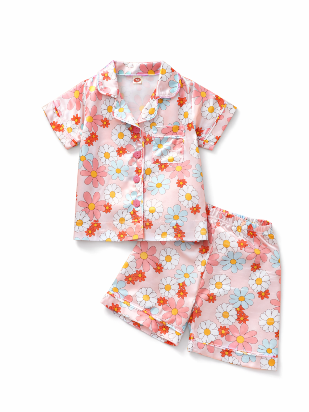 淡いピンクの花柄キッズ用半袖パジャマ上下セット。光沢のある生地で、シャツは前ボタンと胸ポケット付き。白背景にトップスとショートパンツを並べて撮影。
