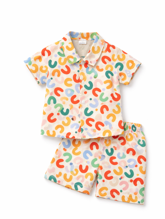 カラフルなU字モチーフの総柄が入った、キッズ用の半袖シャツ＆ショートパンツ上下セット。襟付きの前ボタンシャツと、ウエストゴム仕様のショートパンツを白背景で並べて撮影した商品画像。
