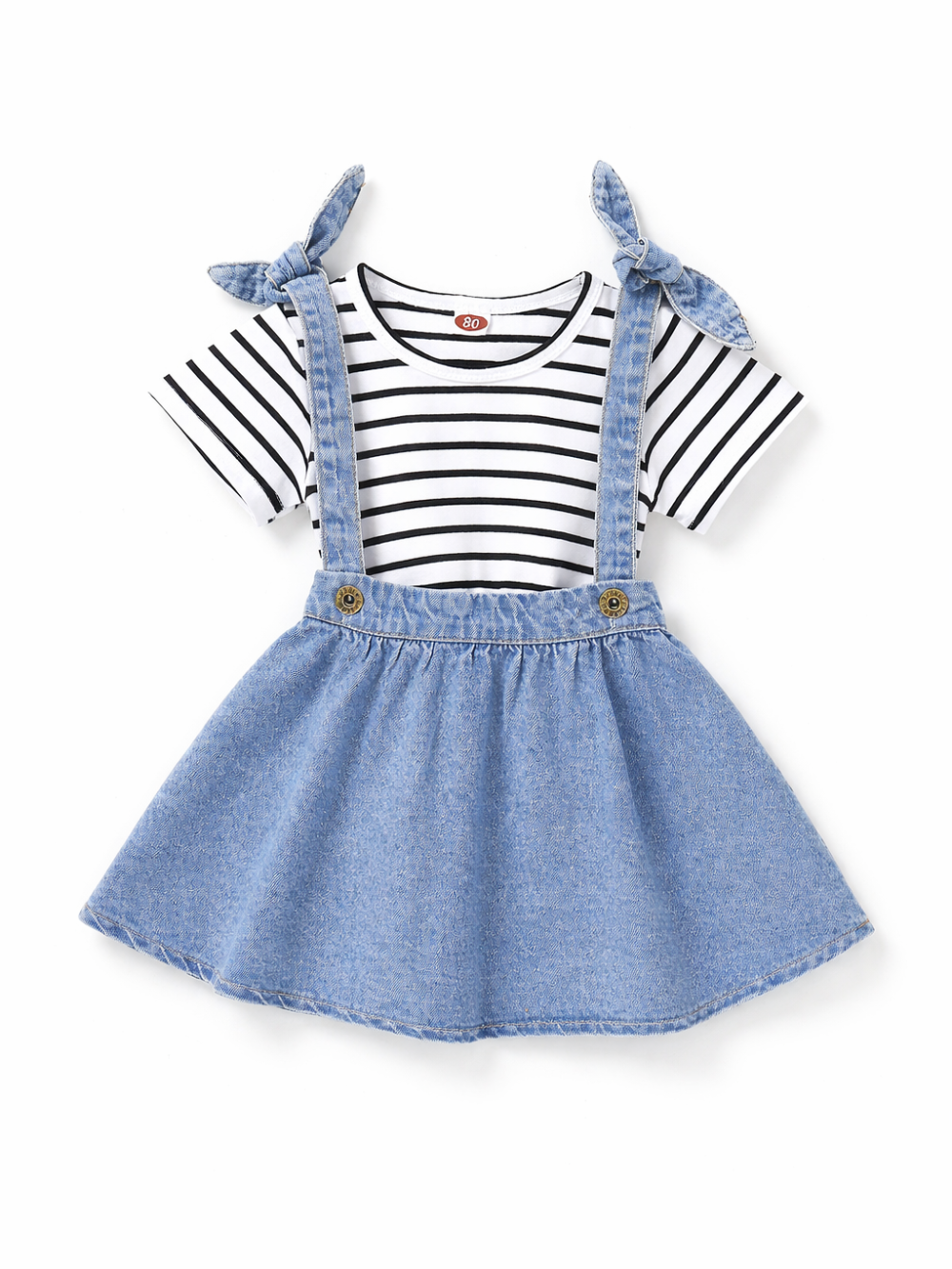 黒×白のボーダー半袖Tシャツに、リボン結びの肩ひも付きライトブルーのデニムジャンパースカートを合わせたキッズセット。白背景のスタジオ撮影で、自然なやわらかい影が入っている。
