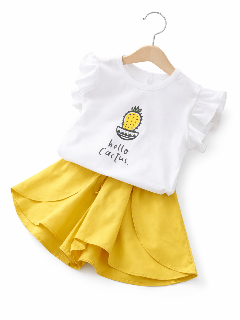 白いフリル袖Tシャツと、マスタードイエローのフレアスカートのキッズセット。Tシャツにはサボテンのイラストと「hello Cactus.」の文字プリント。木製ハンガーに掛けられ、白背景のスタジオ撮影でやわらかな影が入っている。

