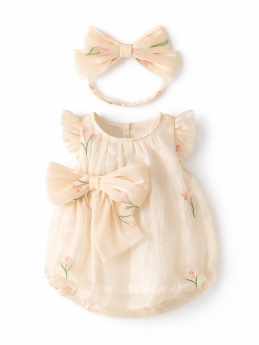 クリーム色のシフォン素材のベビードレスと、同柄の大きなリボン付きヘアバンドを白背景に並べた商品写真。ピンクの小花刺繍とフリル袖、ウエストのリボンが上品に映える。
