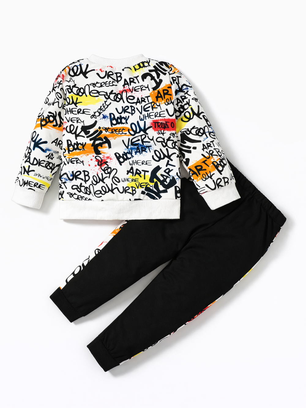 カラフルなグラフィティ風ロゴ総柄のキッズ長袖スウェットと、ブラックのジョガーパンツの上下2点セット。パンツ脇に同柄の切り替えライン入り。白背景のスタジオ撮影。
