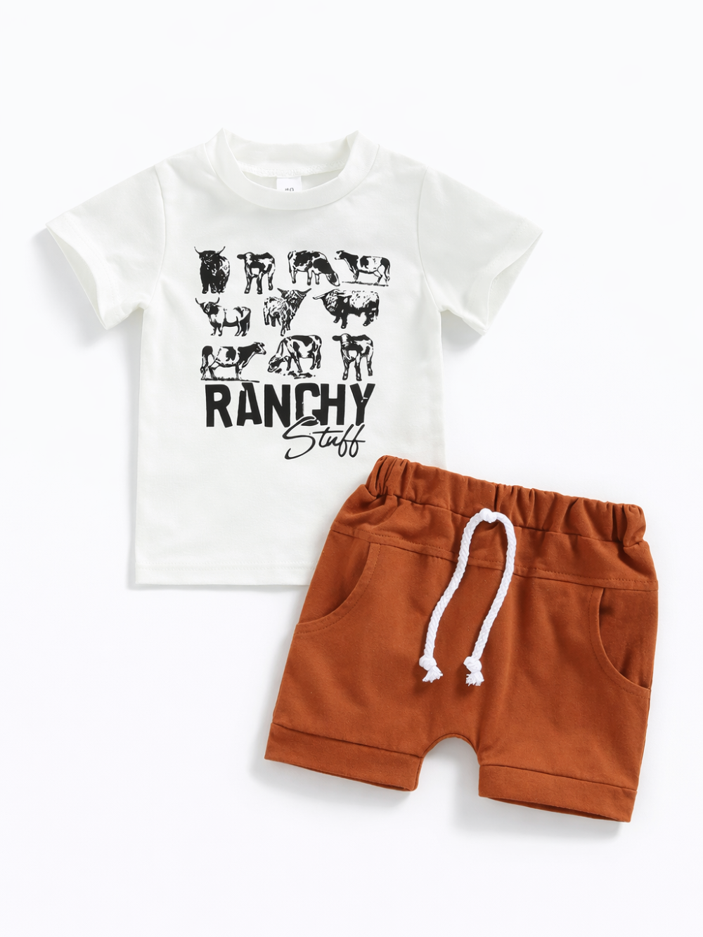牧場モチーフのキッズ上下2点セット。牛のシルエットと「RANCHY Stuff」プリント入りのホワイト半袖Tシャツに、レンガ色のショートパンツ（ウエストゴム・白い紐・ポケット付き）を組み合わせたデザイン。白背景のスタジオ撮影。
