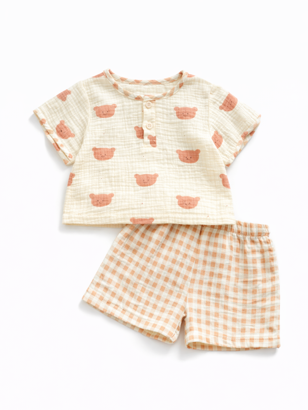 くま顔プリントのキッズ上下2点セット。アイボリーの凹凸素材半袖トップス（前ボタン付き）と、オレンジ×アイボリーのギンガムチェックショートパンツの組み合わせ。白背景のスタジオ撮影。
