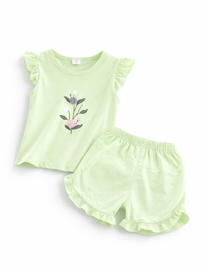 ライトグリーンのキッズ上下2点セット。フリル袖のノースリーブトップスに立体的な花の刺繍モチーフ付きで、ボトムはウエストゴムのフリル裾ショートパンツ。白背景のスタジオ撮影。
