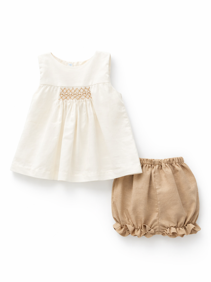 ベビー女の子の2点セット。アイボリーのノースリーブチュニック（胸元スモッキング刺繍入り）と、ベージュのフリル裾ブルマ（ウエストゴム）の組み合わせ。白背景のスタジオ撮影。
