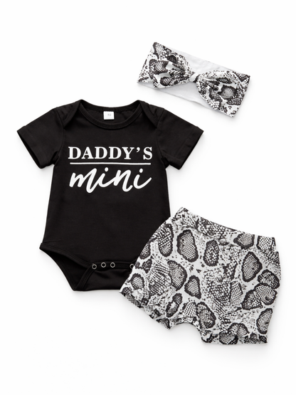 白背景に並べたベビー3点セット。黒の半袖ロンパース（胸元に「DADDY’S mini」プリント）、白黒スネーク柄のブルマ、同柄のリボンヘアバンド。
